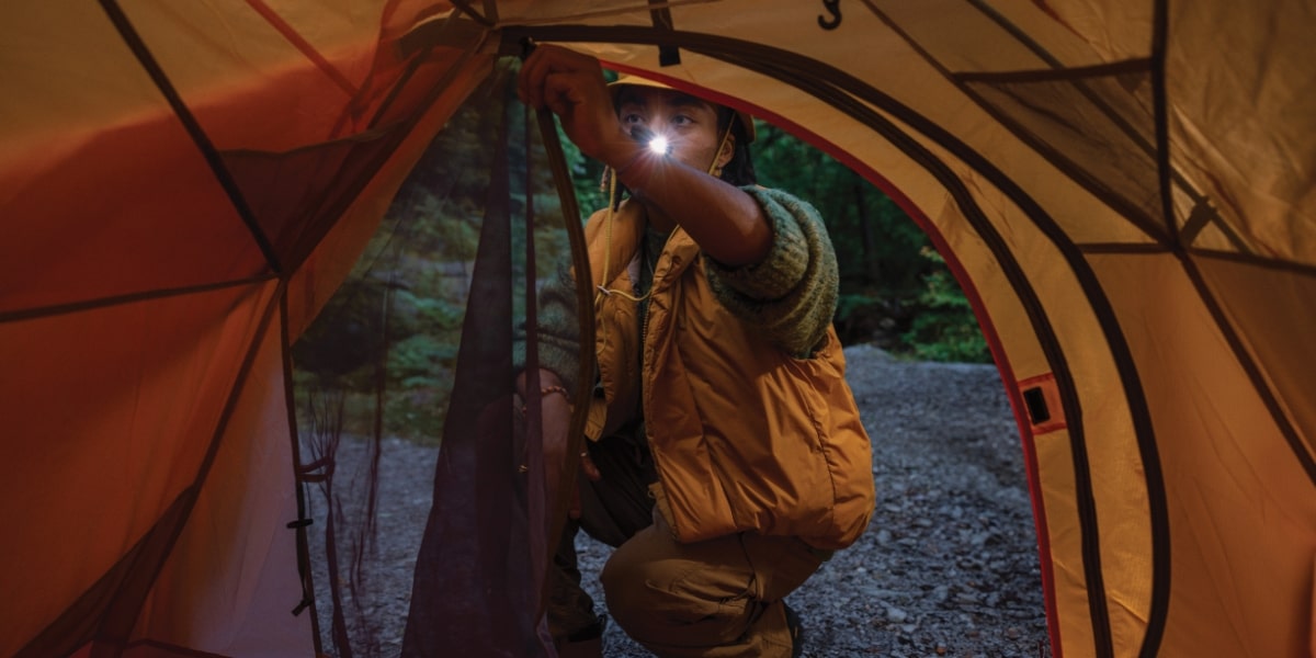 Henkilö teltassa metsäympäristössä ranteessaan Garmin Instinct -kello.