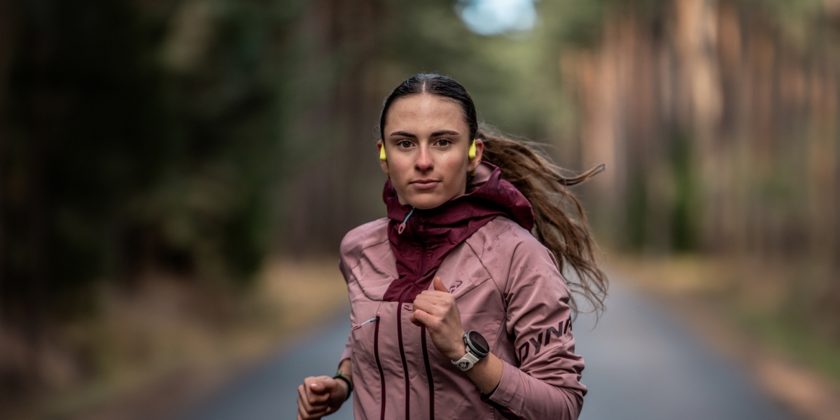 Nainen juoksemassa metsässä yllään korvissaan kirkkaankeltaiset Suunto Sonic luujohdekuulokkeet